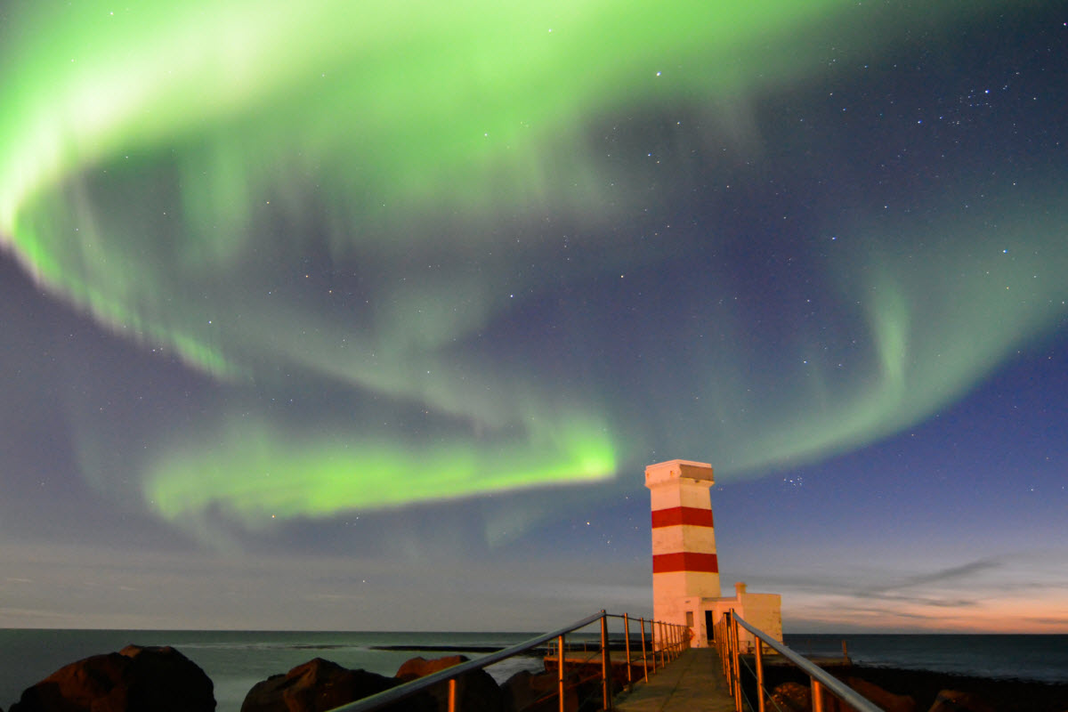 The Northern Lights dancing above the lighthouse in Gardur town, Iceland