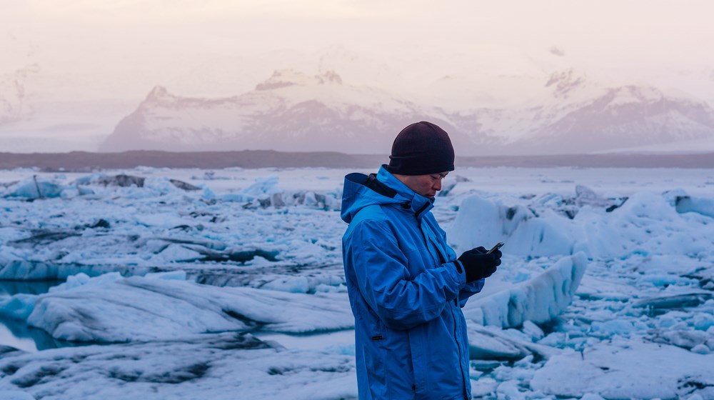 Traveler checking a phone beside Jökulsárlón glacier lagoon