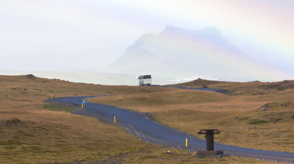 Bus travelling along a rural road beneath a rainbow in South Iceland