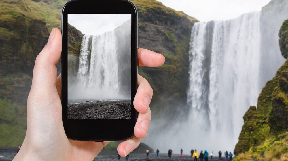 Traveller using a smartphone at Skógafoss waterfall in South Iceland