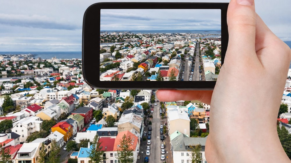 A traveller photographing Reykjavík, with the city visible on the smartphone screen