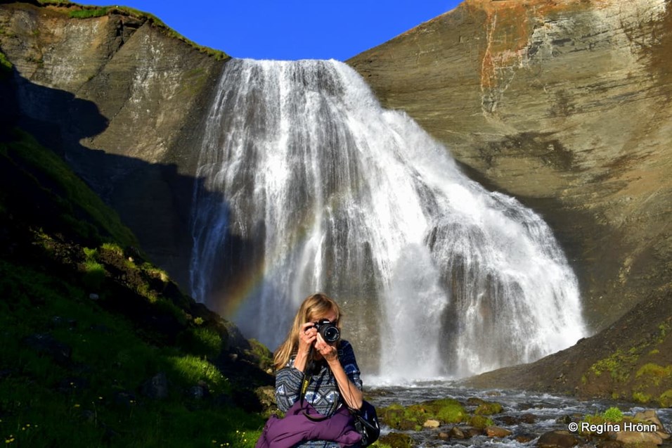 Woman taking a photo with a waterfall behind her